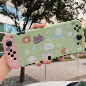 Può includere: Una custodia per Nintendo Switch verde e rosa a tema baseball. La custodia presenta una varietà di personaggi dei cartoni animati carini, tra cui gatti, un coniglio e una palla da baseball. Il testo "Baseball Championship" è stampato sulla custodia.