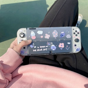 K&ouml;nnte beinhalten: Eine graue Nintendo Switch-Konsole mit einer transparenten Schutzh&uuml;lle. Die H&uuml;lle ist mit Aufklebern von V&ouml;geln, Blumen und B&auml;umen verziert. Der Text "A Story of the Blue Sky" ist auf der H&uuml;lle aufgedruckt.