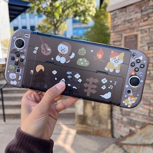 May include: A brown and black Nintendo Switch case with a camping theme. The case features a variety of cute animal stickers, including a dog, a cat, and a bird. The case also has a variety of other stickers, including trees, a campfire, and a sign that says "Nintendo Switch".