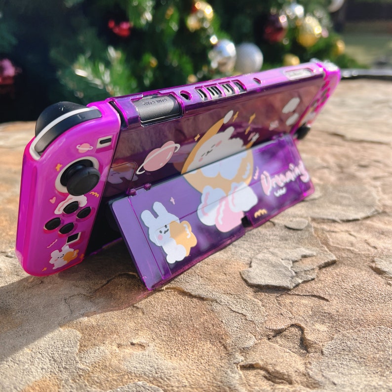 May include: A purple and white Nintendo Switch case with a stand. The case has a cartoon design with a bunny and the word "Dreaming".