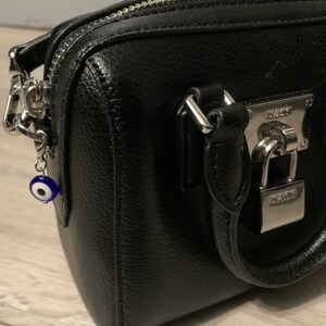 May include: A black leather handbag with a silver lock and chain strap. A blue and white evil eye charm hangs from the strap.