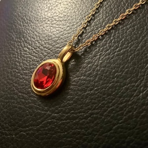 May include: A gold chain necklace with a pendant featuring a large, oval-shaped red gemstone.