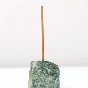 May include: A brown incense stick standing upright in a green stone holder.