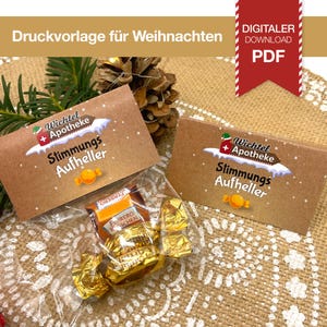 May include: A clear cellophane bag filled with gold-wrapped chocolates and Ferrero Rocher candies, with a brown card that reads "Wichtel + Apotheke Stimmungs Aufheller". The image also includes a red PDF download graphic.