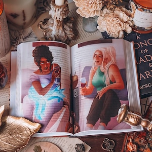 May include: An open book with illustrations of two women drinking wine. The book is surrounded by candles, flowers, and decorative keys. The artwork features a fantasy theme with a soft color palette.