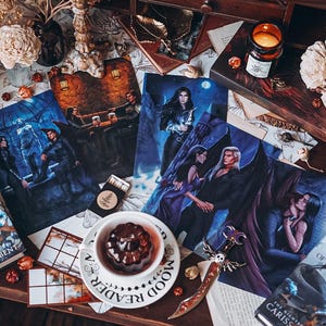 May include: A collection of fantasy book covers featuring dark blue and purple hues, with illustrations of characters and scenes. The covers are displayed on a wooden table with a cup of tea, a decorative sword, and a book titled "The Night Without Stars" by Carissa Broadbent.
