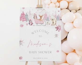 May include: Welcome to Madison's Baby Shower sign with a winter wonderland theme. The sign features a pink sleigh with a penguin, a deer, and a polar bear. The sign is decorated with snowflakes and a pink and white color scheme.
