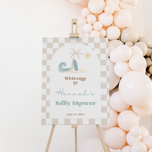 May include: A welcome sign for a baby shower with a checkered background and a beach scene with a palm tree, surfboard, and wave. The text reads "Welcome to Hannah's Baby Shower July 13, 2024".