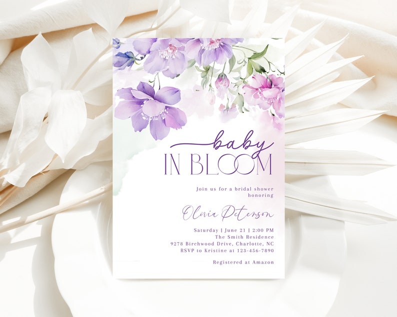 May include: A purple and white floral bridal shower invitation with the text "baby in bloom" and the name "Olivia Peterson". The invitation includes the date, time, location, and RSVP information. It also states that the guest of honor is registered at Amazon.