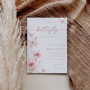 May include: A white baby shower invitation with pink butterflies and flowers. The text reads "A little butterfly is on the way."  Join us for a baby shower in honor of Olivia Johnson. Saturday, March 5 1:2PM. The Smith Residence. 7204 Birchwood Drive. RSVP to Kristine at 123-456-7890. Registered at Babylist.
