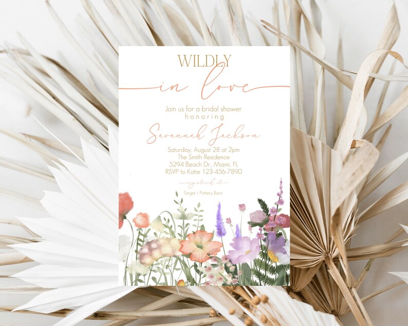 May include: A white bridal shower invitation with gold lettering that reads "WILDLY in love" and features a watercolor illustration of a bouquet of pink, purple, and orange flowers. The invitation includes the bride's name, the date and time of the shower, the location, and RSVP information.