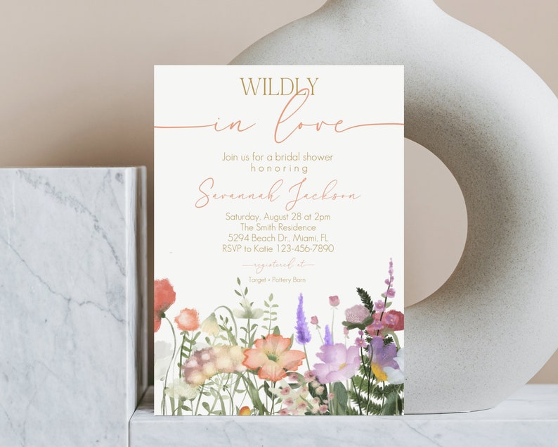 May include: A white bridal shower invitation with a floral border. The invitation reads "WILDLY in love" and includes the text "Join us for a bridal shower honoring Savannah Jackson". The invitation also includes the date, time, location, and RSVP information.
