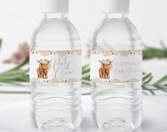 以下が含まれることがあります： ラベルが付いた透明なプラスチック製の水筒が2本。ラベルには、花輪をつけたハイランド牛の水彩画が描かれています。ラベルのテキストは「Holy Cow」と「Madison's Baby Shower」です。