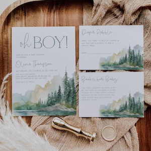 a baby shower invitation with a forest landscape design, a gold wax seal, and a small decorative item.