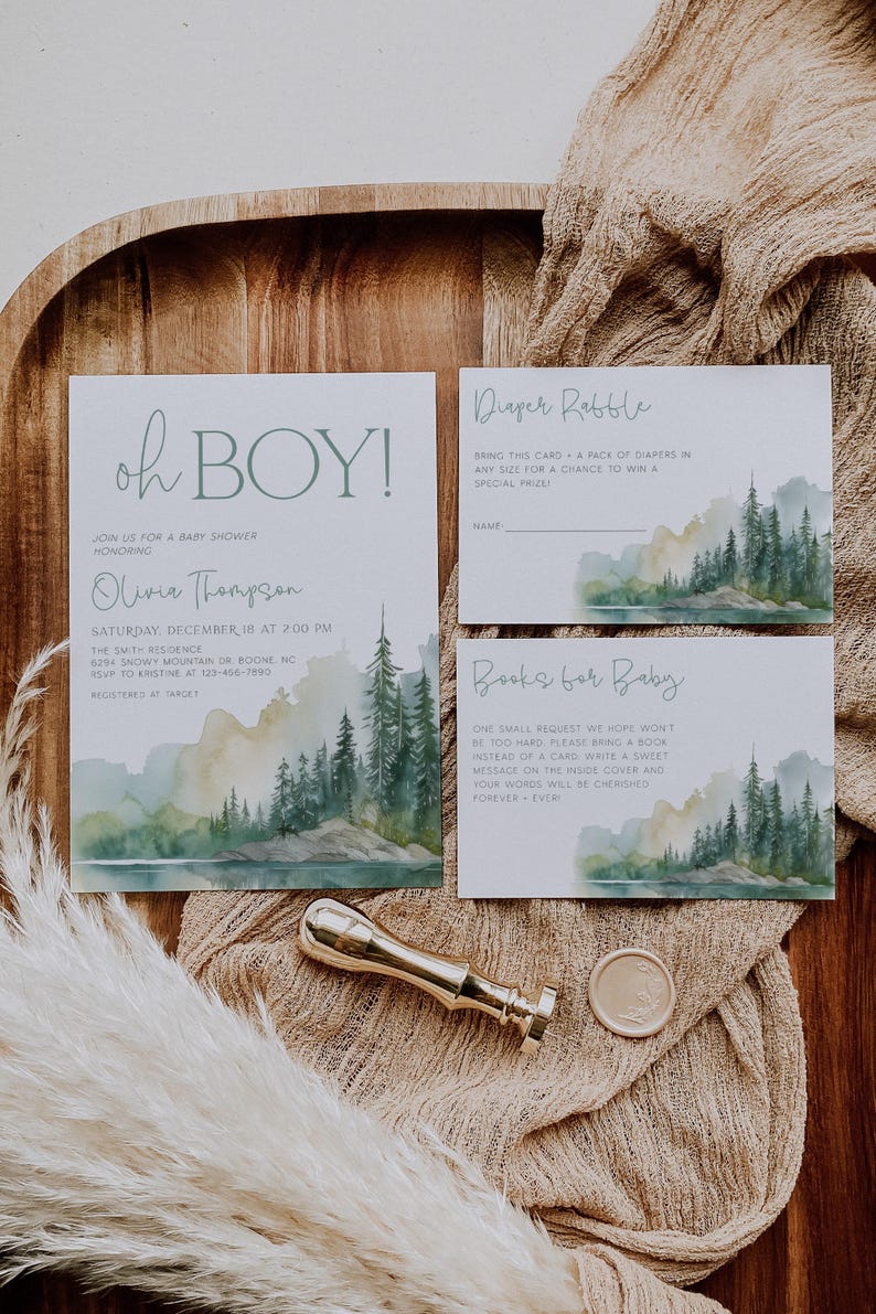 a baby shower invitation with a forest landscape design, a gold wax seal, and a small decorative item.