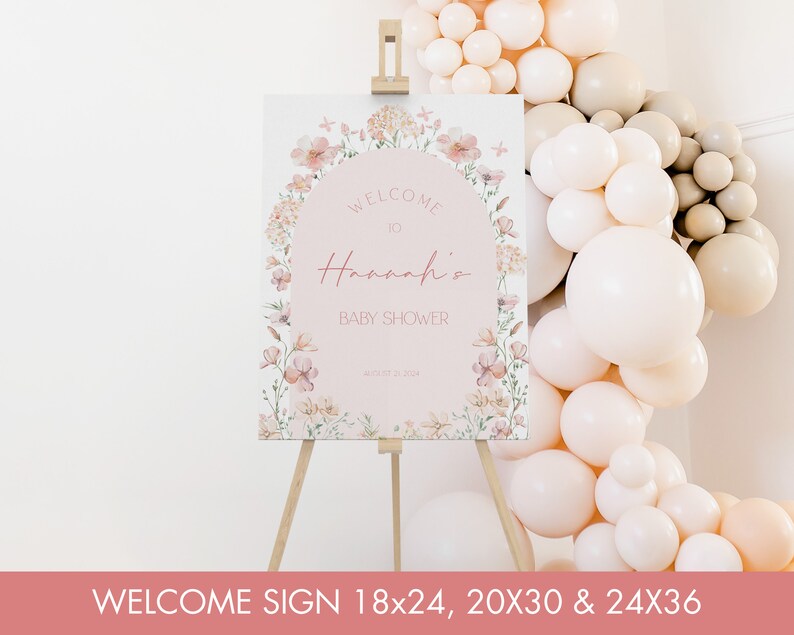 May include: A welcome sign for a baby shower featuring a floral design. The sign is pink with a white circle in the centre that says "Welcome to Hannah's Baby Shower".