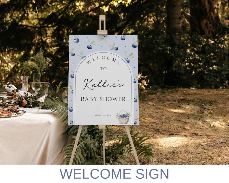 May include: A blue and white welcome sign with a watercolor blueberry design. The sign reads "Welcome to Kallie's Baby Shower, August 18, 2024".