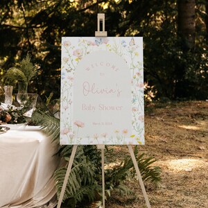 Puede incluir: Un cartel de bienvenida para un baby shower con un diseño floral y mariposas. El cartel dice "Bienvenido a Olivia's Baby Shower 21 de marzo de 2024".