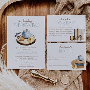 Op de afbeelding: Een set van drie witte papieren kaarten voor een babyshower met aquarelillustraties van een blauwe mok, pompoenen en boeken. De tekst luidt A BABY IS BREWING, BOOKS FOR BABY en DIAPER RAFFLE met evenementdetails en instructies.