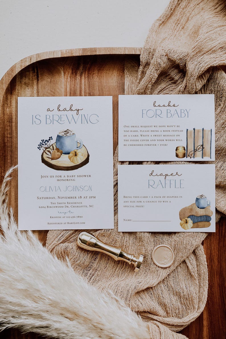 Op de afbeelding: Een set van drie witte papieren kaarten voor een babyshower met aquarelillustraties van een blauwe mok, pompoenen en boeken. De tekst luidt A BABY IS BREWING, BOOKS FOR BABY en DIAPER RAFFLE met evenementdetails en instructies.