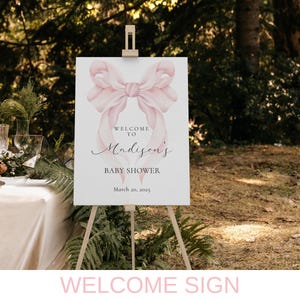 May include: Welcome sign for a baby shower with a pink watercolor bow and the text "Welcome to Madison's Baby Shower March 20, 2023".