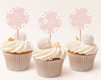 May include: Three cupcakes with white frosting, each topped with a decorative pink circle. The circles feature daisy designs and text that reads "Happy Birthday Charlotte", "ONE Happy Day", and "Charlotte's 1st Birthday".