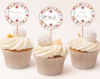 May include: Three cupcakes decorated with white frosting and topped with a coconut ball and a gold star. Each cupcake has a round floral-themed paper topper with the text "Everly's 1st Birthday", "ONE", and "Happy Birthday Everly".
