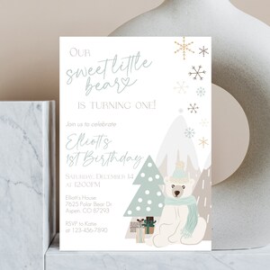 May include: A birthday invitation featuring a polar bear wearing a hat and scarf, with a Christmas tree and mountains in the background. The text reads "Our Sweet Little Bear is Turning One!" and includes event details.