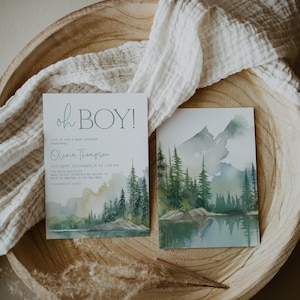 a wooden bowl with two printed cards, one of which is a baby shower invitation with a mountain landscape design.