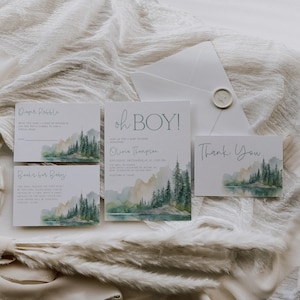 A collection of wedding invitations and thank-you cards, featuring a scenic mountain landscape, arranged on a white fabric background.