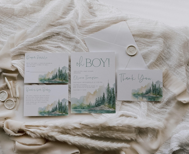A collection of wedding invitations and thank-you cards, featuring a scenic mountain landscape, arranged on a white fabric background.