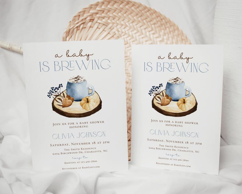 Op de afbeelding: Twee witte uitnodigingskaarten voor een babyshower met de tekst 'a baby IS BREWING' in bruin en blauw. Het ontwerp bevat een aquarelillustratie van een blauwe mok, een kleine pompoen en bessen op een houten schijf. Details bevatten de naam Olivia Johnson, datum, tijd en locatie.