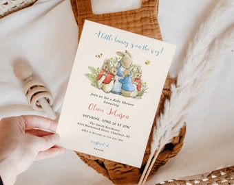 Może przedstawiać: Zaproszenie na baby shower z akwarelową ilustracją Piotrusia Królika i jego rodziny. Zaproszenie zawiera napis "Mały króliczek jest w drodze!" i zawiera szczegóły baby shower, w tym datę, godzinę, miejsce i informacje RSVP. Zaproszenie jest zarejestrowane na Amazon.