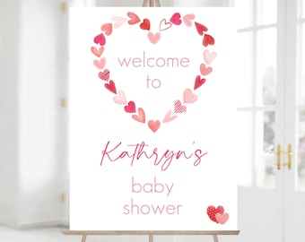Könnte beinhalten: Ein weißes Willkommens-Schild mit einem rosa Herz aus kleineren rosa Herzen. Der Text lautet "Willkommen zu Kathryns Babyparty".