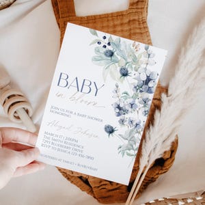 a hand holding a baby shower invitation with a floral design.
