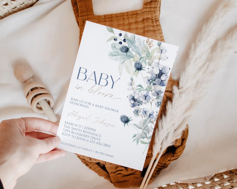 a hand holding a baby shower invitation with a floral design.