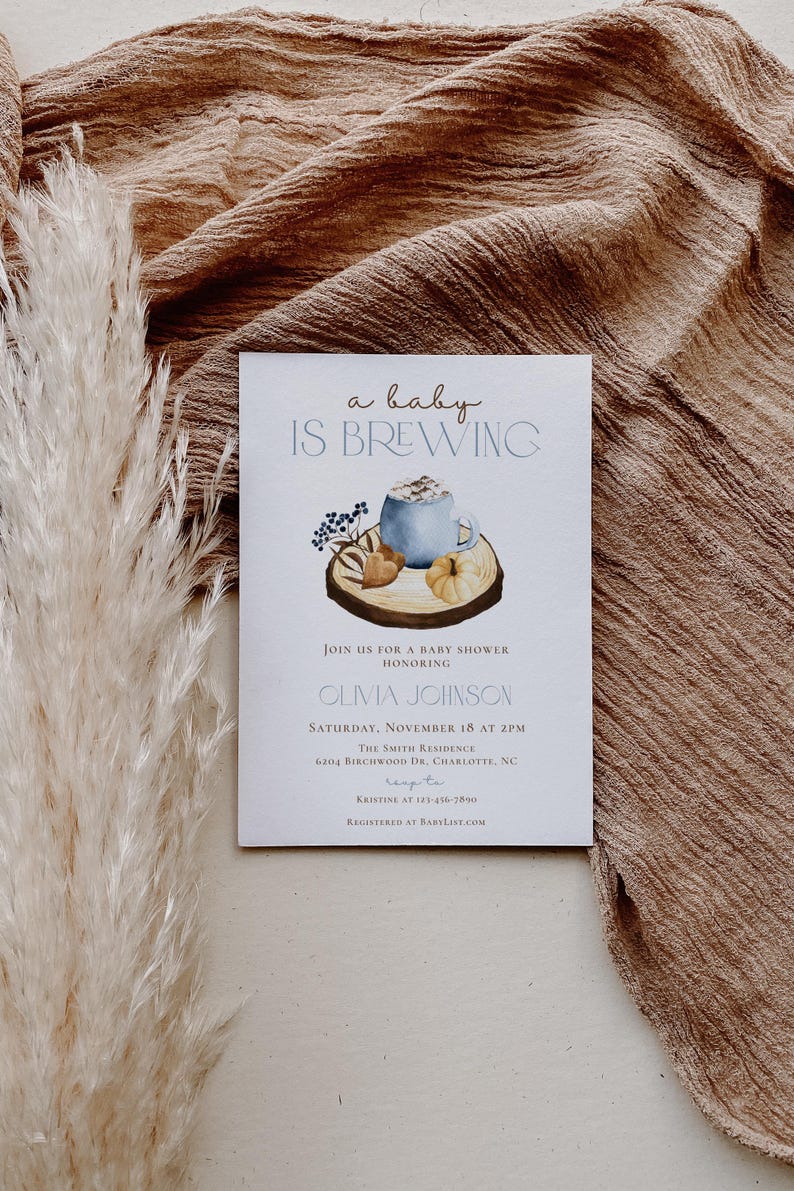 Op de afbeelding: Een witte rechthoekige uitnodigingskaart voor een babyshower met de tekst a baby IS BREWING en een aquarelillustratie van een blauwe mok, een pompoen en bessen op een houten schijf. De kaart bevat de evenementgegevens voor Olivia Johnson op 18 november.