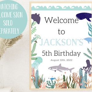 May include: A welcome sign for a 5th birthday party with an under the sea theme. The sign is white with blue text and features illustrations of sea creatures like a whale, jellyfish, and an octopus. The text reads "Welcome to Jackson's 5th Birthday August 12th, 2022".