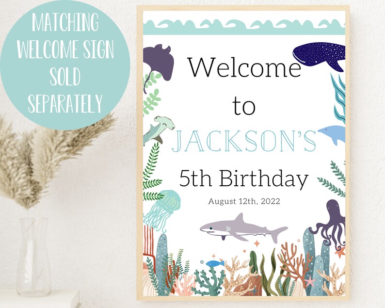 May include: A welcome sign for a 5th birthday party with an under the sea theme. The sign is white with blue text and features illustrations of sea creatures like a whale, jellyfish, and an octopus. The text reads "Welcome to Jackson's 5th Birthday August 12th, 2022".