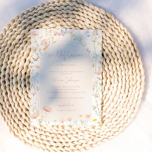 May include: A baby shower invitation with a floral design featuring pink, yellow, and blue wildflowers and butterflies. The text on the invitation reads "Our Little Wildflower" and includes the name "Olivia Johnson" and the date "Saturday, March 21st at 2 PM".