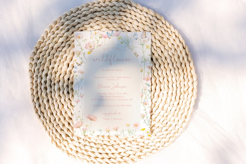 May include: A baby shower invitation with a floral design featuring pink, yellow, and blue wildflowers and butterflies. The text on the invitation reads "Our Little Wildflower" and includes the name "Olivia Johnson" and the date "Saturday, March 21st at 2 PM".