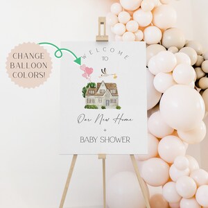 Puede incluir: Bienvenido a nuestro nuevo hogar + Baby Shower cartel con una ilustraci&oacute;n de una casa y una cig&uuml;e&ntilde;a. El cartel est&aacute; en un caballete de madera frente a un arco de globos.