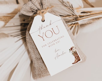 May include: A burlap bag tied with twine, featuring a white tag with the words "thank YOU" in a stylish font. The tag includes the text "FOR CELEBRATING WITH US!" and "love, Amelia." A brown cowboy boot with flowers is illustrated on the tag.