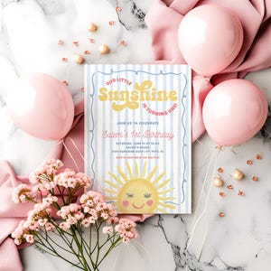 May include: A birthday invitation with the text "Our Little Sunshine is Turning One!" in yellow and blue. The invitation features a smiling sun illustration and is surrounded by pink balloons and flowers.