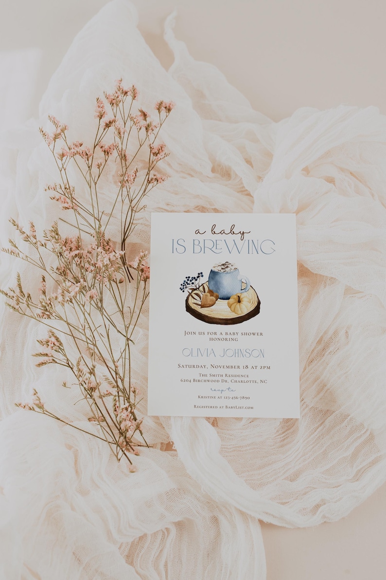 Op de afbeelding: Een witte rechthoekige uitnodigingskaart voor een babyshower met de tekst 'a baby IS BREWING' boven een aquarelillustratie van een blauwe mok, een kleine pompoen en bessen op een houten schijf. De kaart bevat details over het evenement.