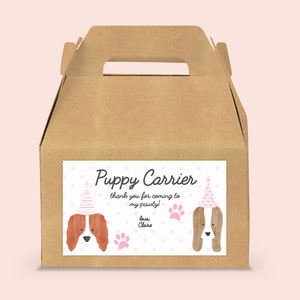 May include: A brown cardboard box with a handle, labeled "Puppy Carrier" with a pink and white polka dot background. The label features two cartoon dogs wearing pink party hats. The text on the label reads "Thank you for coming to my pawty! Love, Claire."