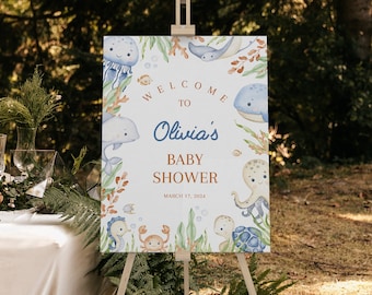 May include: Welcome to Olivia's Baby Shower sign with a blue and white watercolor design featuring sea creatures like a whale, octopus, jellyfish, and seahorse. The sign is on a wooden easel and has the date March 17, 2024.