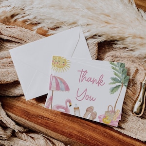 Puede incluir: Un juego de tarjetas de "Gracias" con un sobre a juego. Las tarjetas presentan una ilustraci&oacute;n de acuarela de una escena de playa con un sol, una sombrilla, un flamenco y una palmera. El texto "Gracias" est&aacute; escrito en rosa.