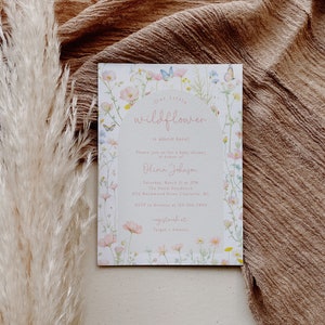 May include: A baby shower invitation with a floral design featuring pink and white wildflowers, butterflies, and the text "Our Little Wildflower is almost here!"  Please join us for a baby shower in honor of Olivia Johnson. Saturday, March 21 at 2PM. The Smith Residence. 4712 Birchwood Drive Charlotte, NC. RSVP to Kristine at 123-456-7890. Registered at Target - Amazon.