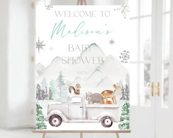 May include: Welcome to Madison's Baby Shower sign with a watercolor illustration of a white truck with a deer, fox, bear, and squirrel on top, driving through a snowy mountain landscape. The date 12.17.22 is printed below the words "Baby Shower".